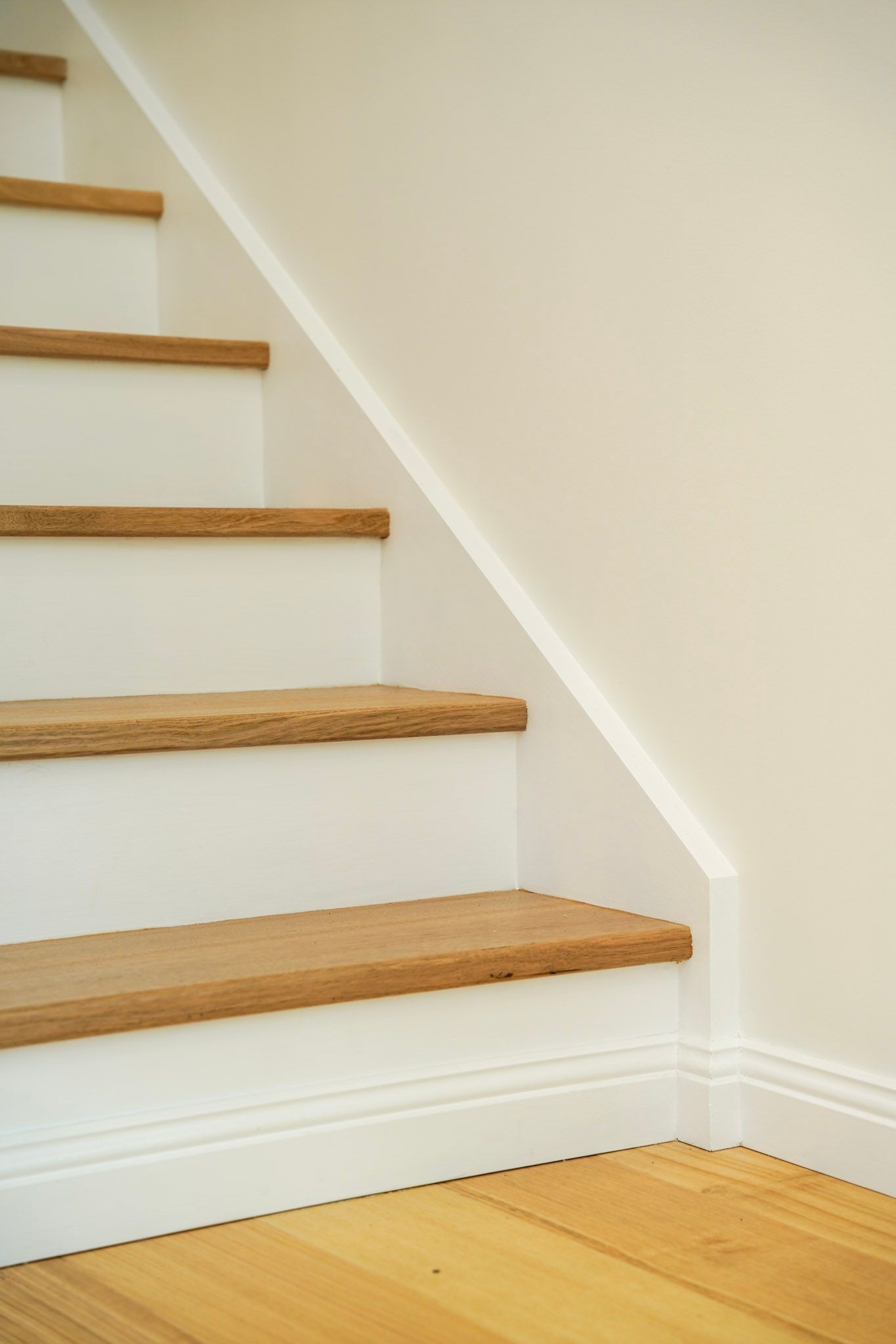 Wooden staircase with white risers and trim, wood treads, against a cream-colored wall.