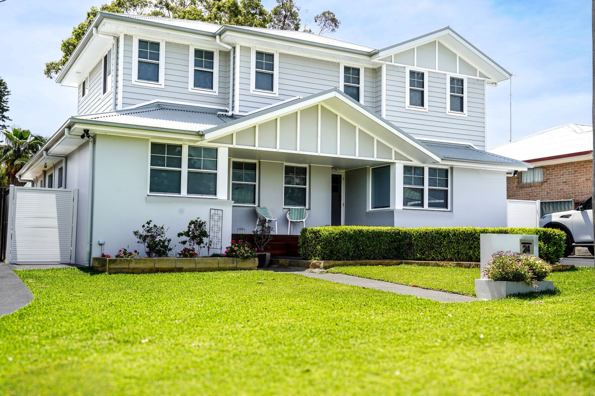 Two-story gray house with white trim, green lawn, and hedge.