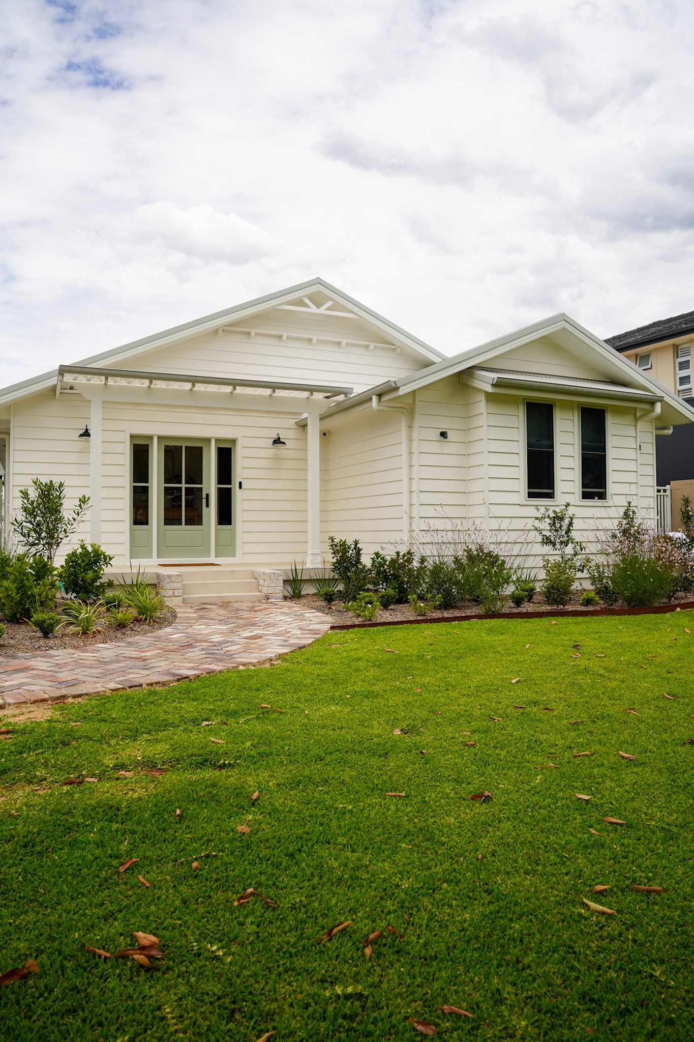 White house with green door, windows, and decorative trim. A brick walkway and grassy yard are in front.
