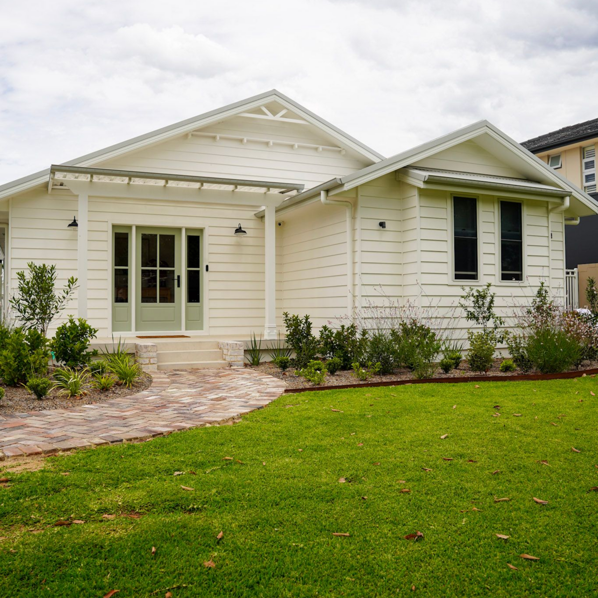 White house with green door, brick walkway, and green lawn under a cloudy sky.