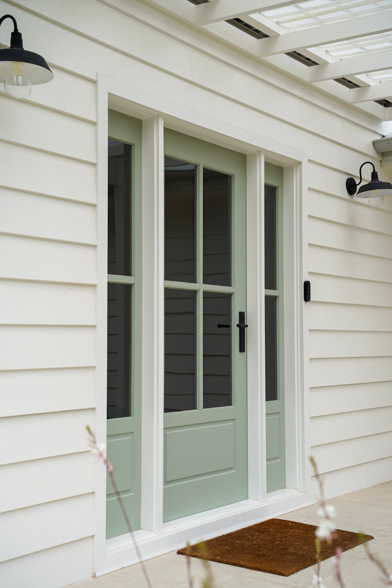 A light green door with glass panels framed by white siding, exterior lighting.