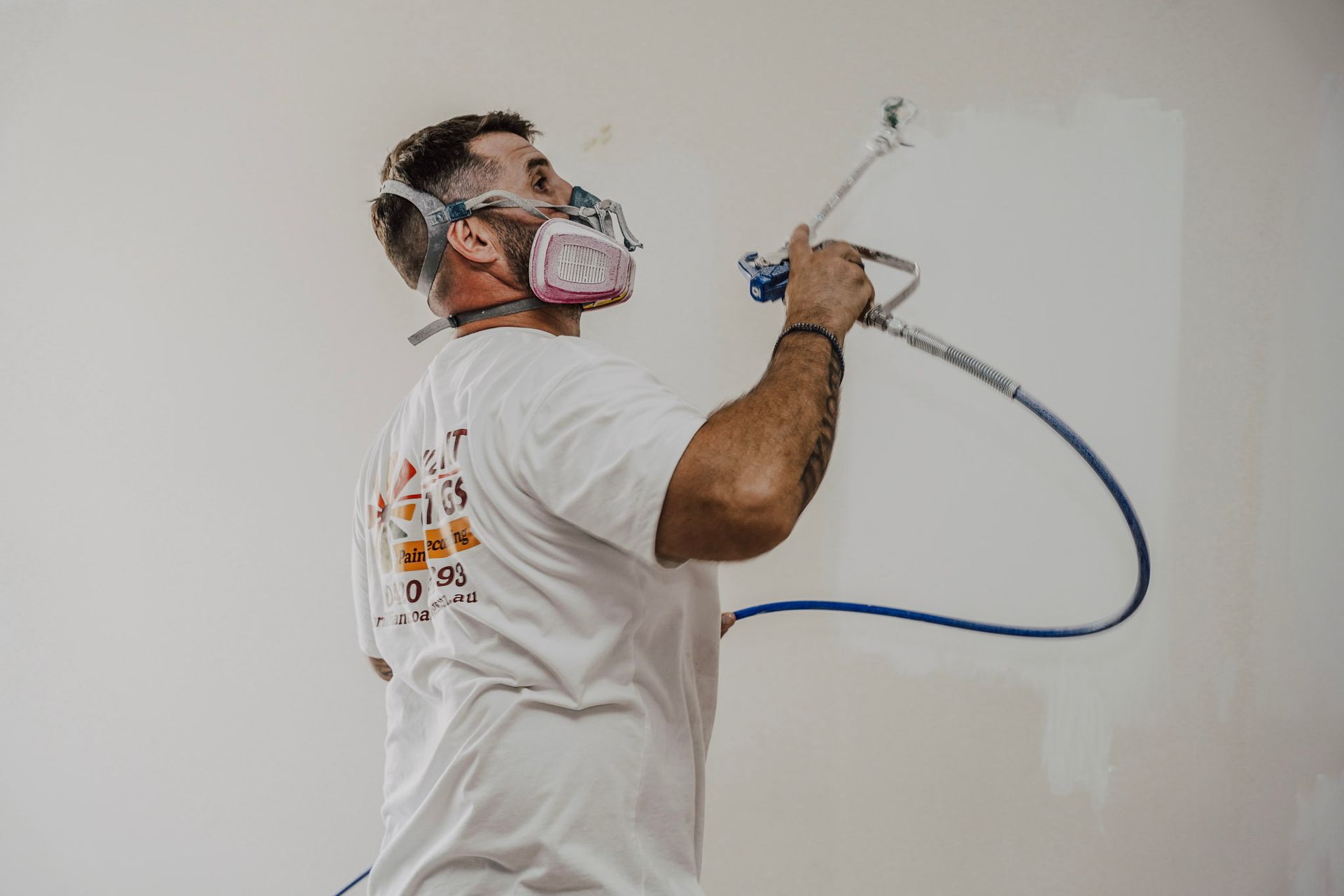 Man wearing respirator spraying paint on a white wall.