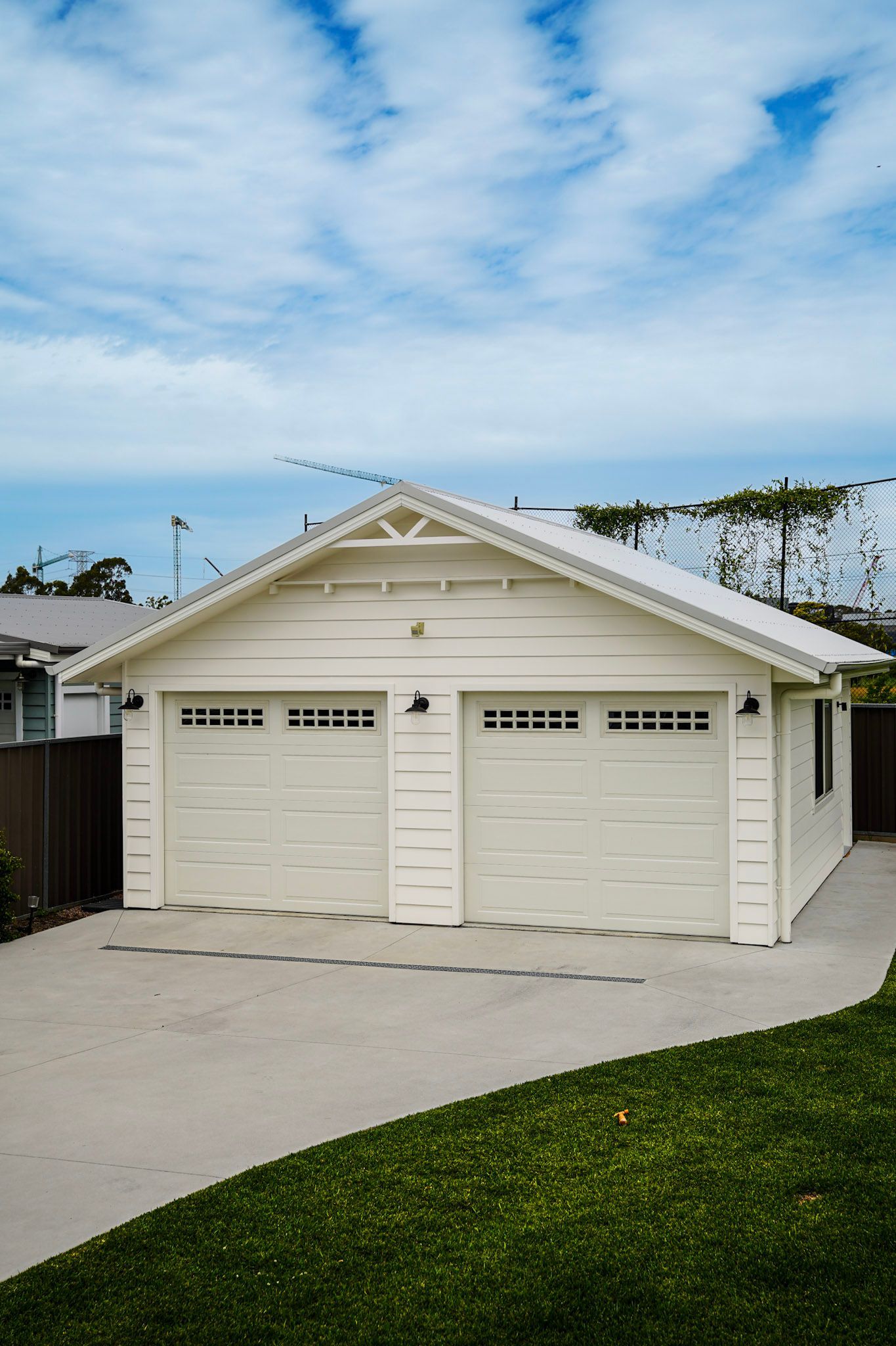 White two-car garage with matching doors on a concrete driveway, under a cloudy blue sky.