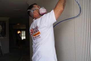 Man wearing a respirator spraying a wall with a paint sprayer, indoors.