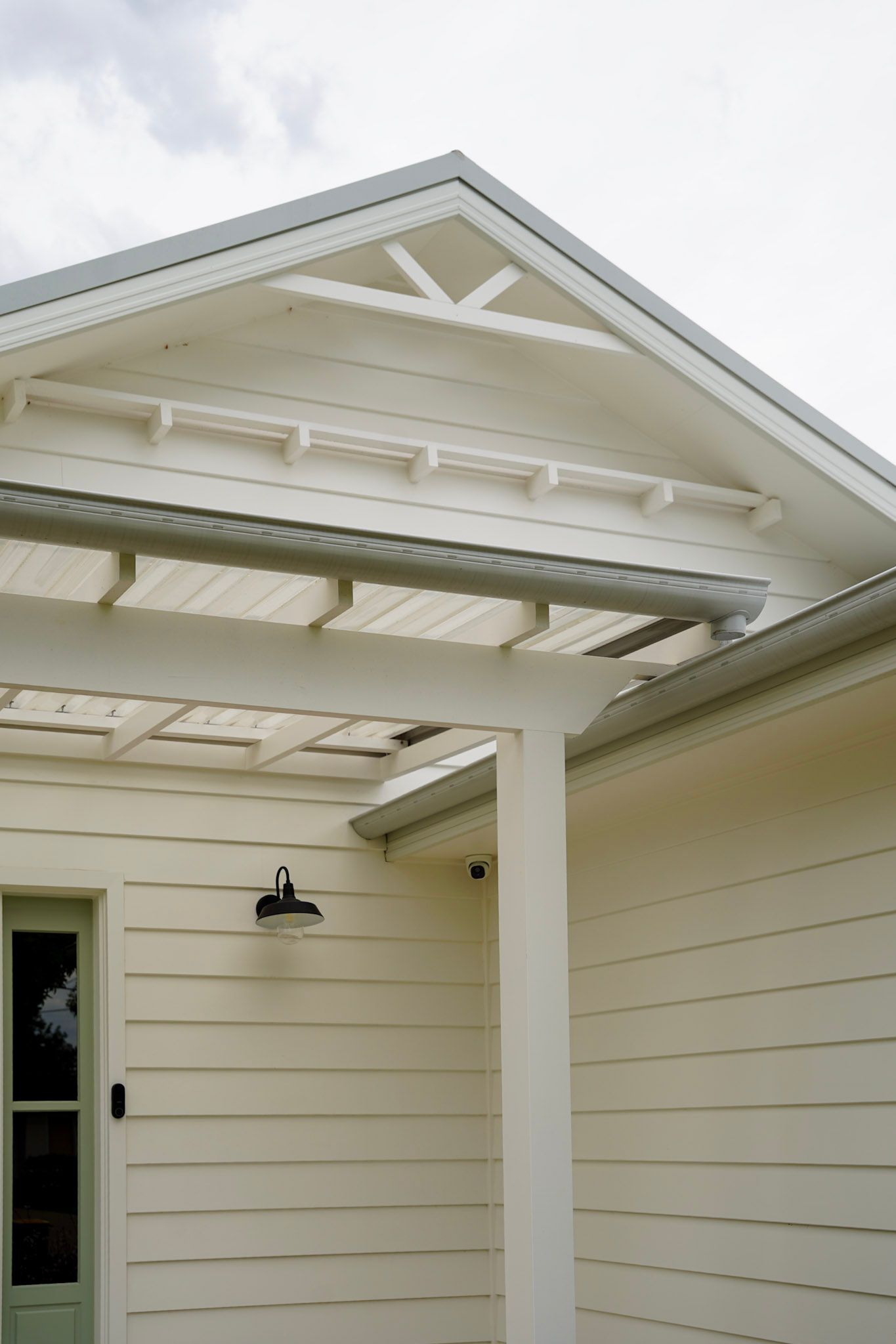 White house exterior with decorative gable, pergola, and light-colored siding.