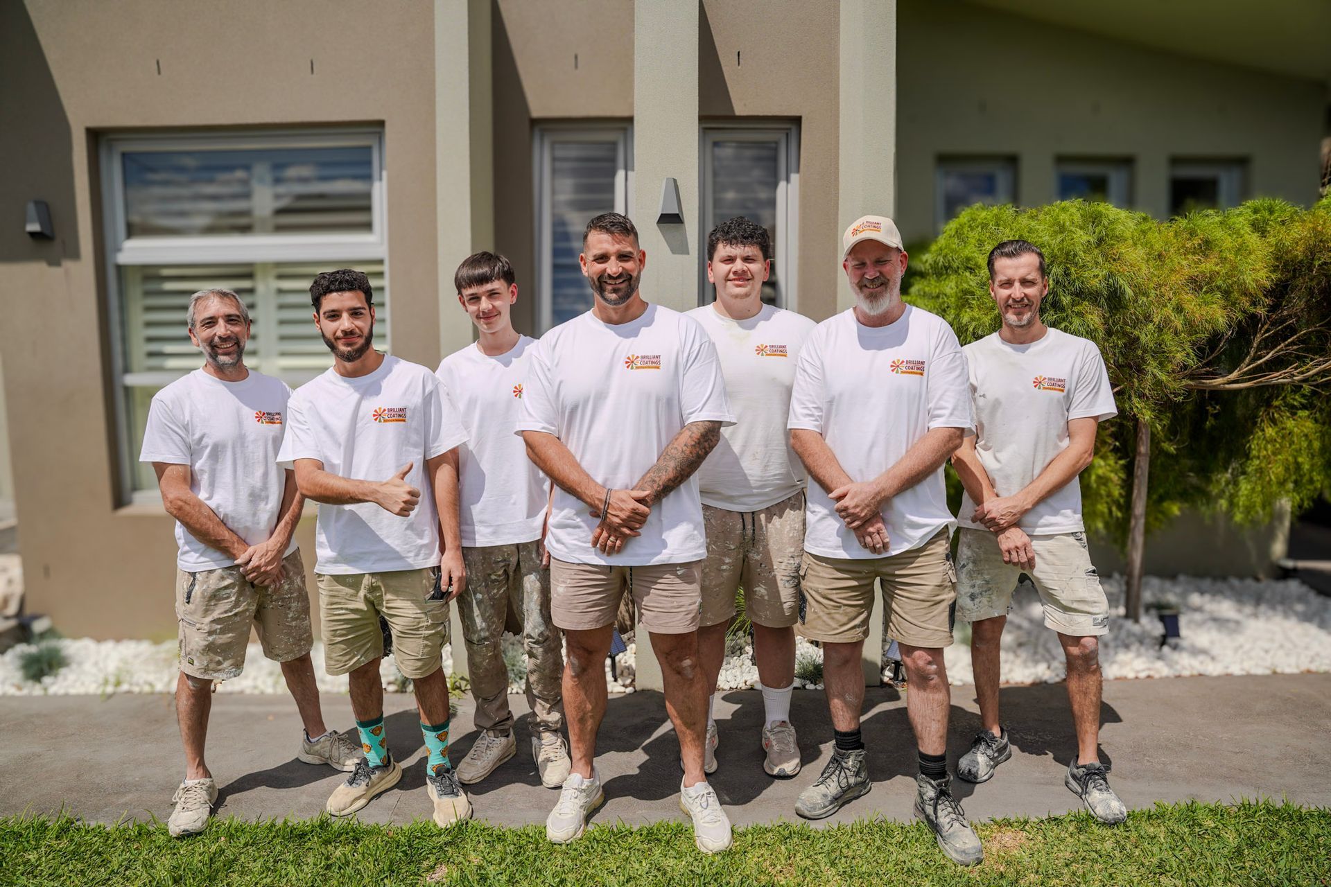 Group of seven people wearing white shirts and shorts posing outside a modern building.
