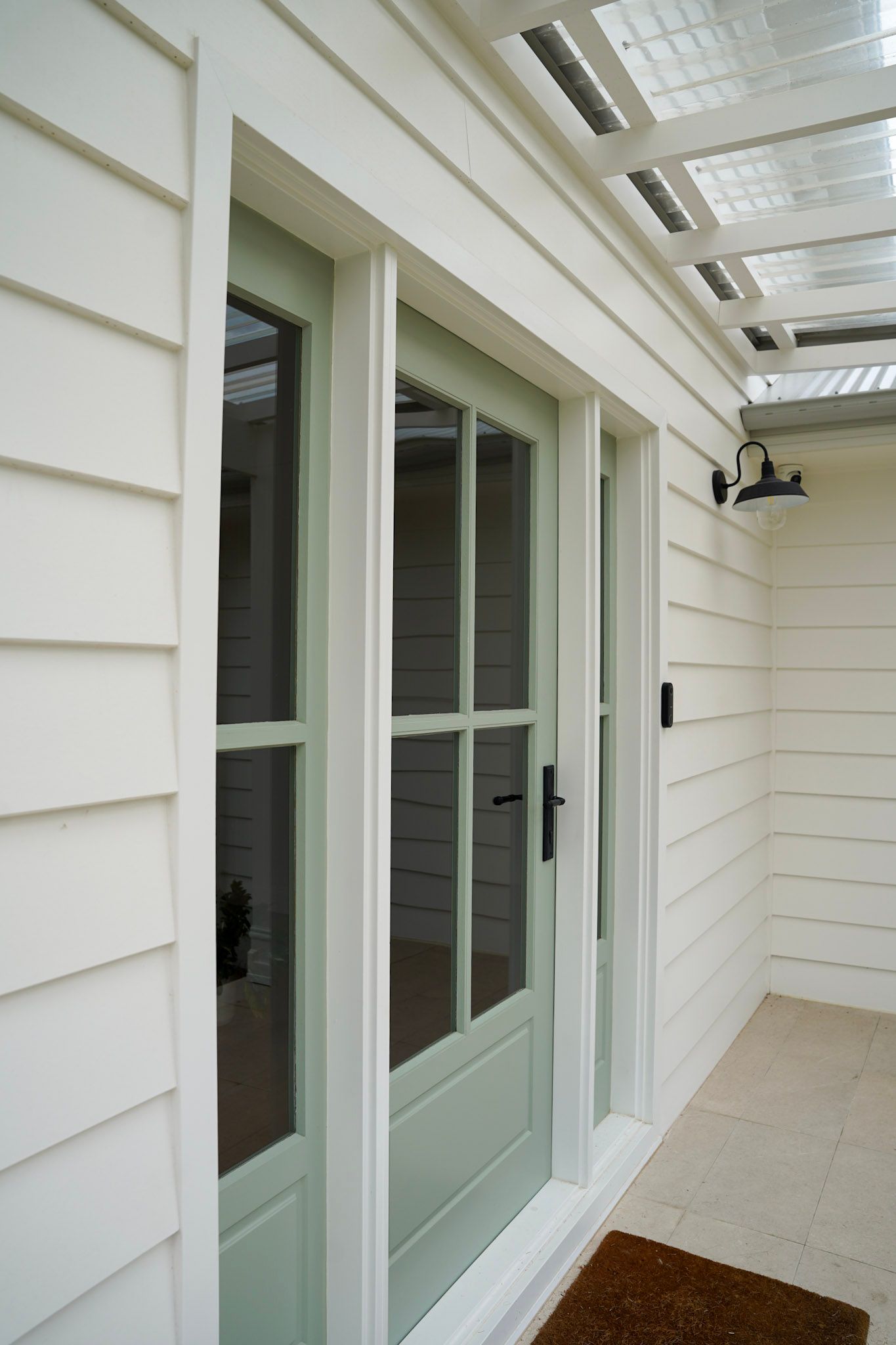 White house exterior with a green door, glass panels, and a small awning.