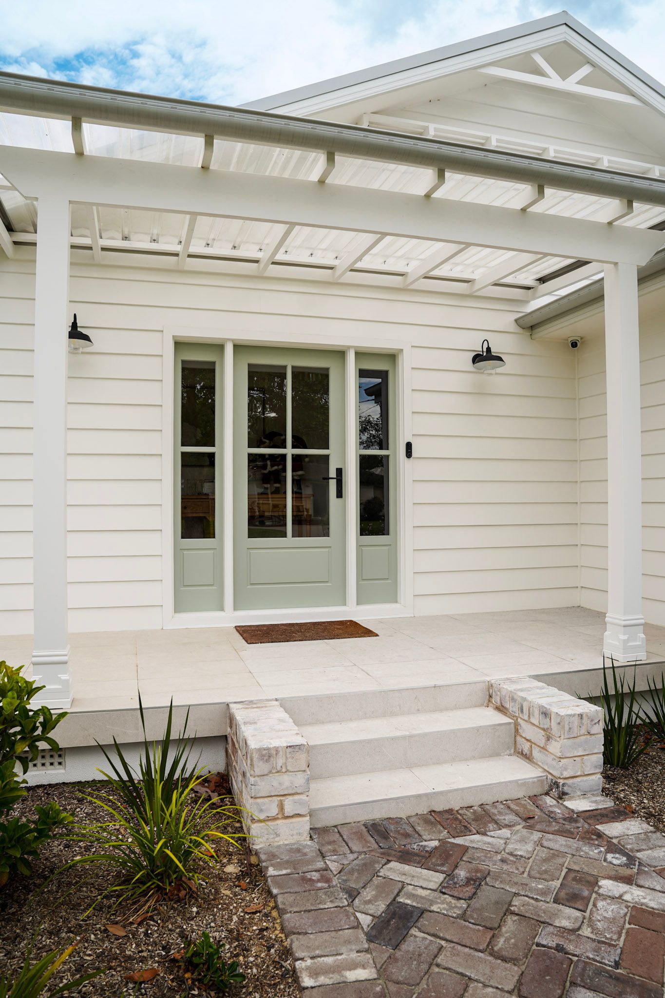 White house entrance with green door and pergola, stone steps, and brick walkway.