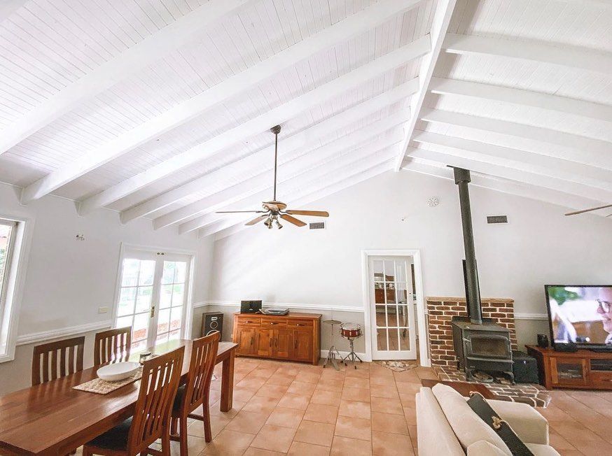 White-painted tongue-and-groove ceiling in a dining/living room with a wooden table, chairs, and a fireplace.