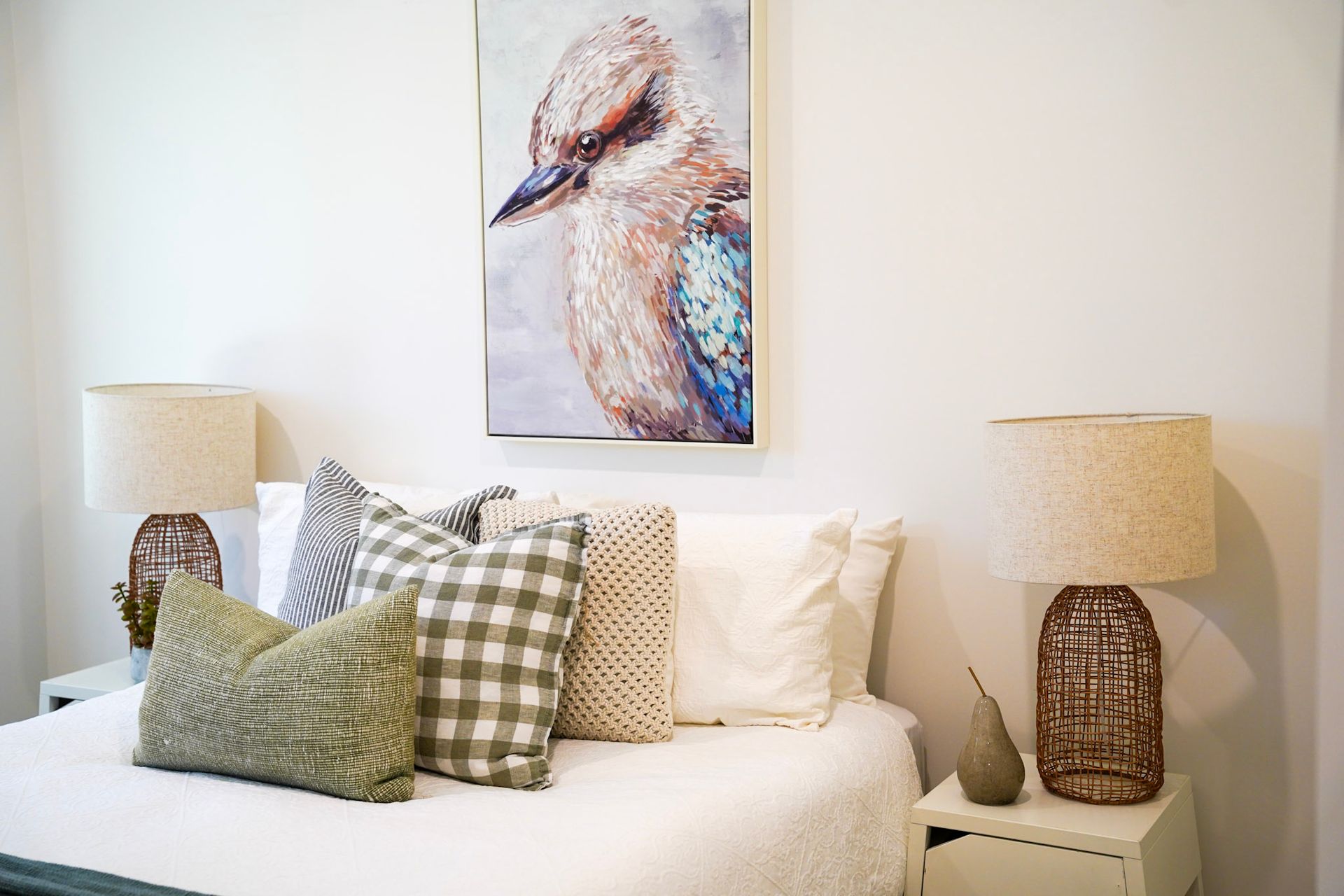 Bedroom with white bedding, pillows, art of a bird, and bedside lamps.