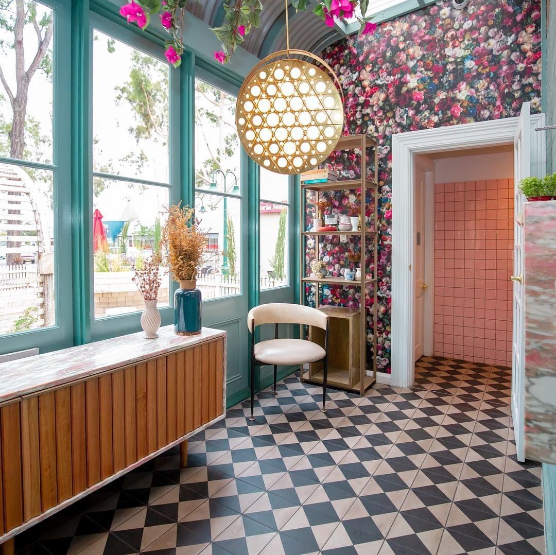 Interior room with floral wallpaper, black and white checkered floor, wooden cabinet, chair, and gold chandelier.