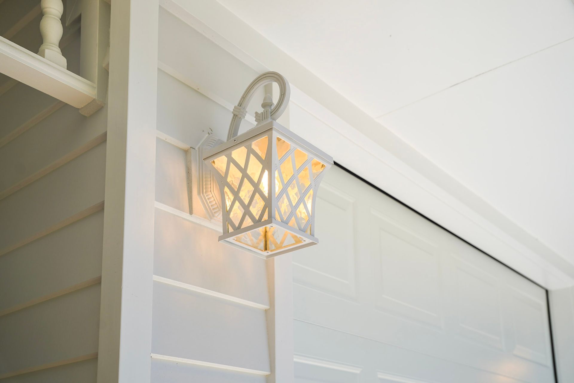 White decorative lantern on a white wall, emitting warm light.