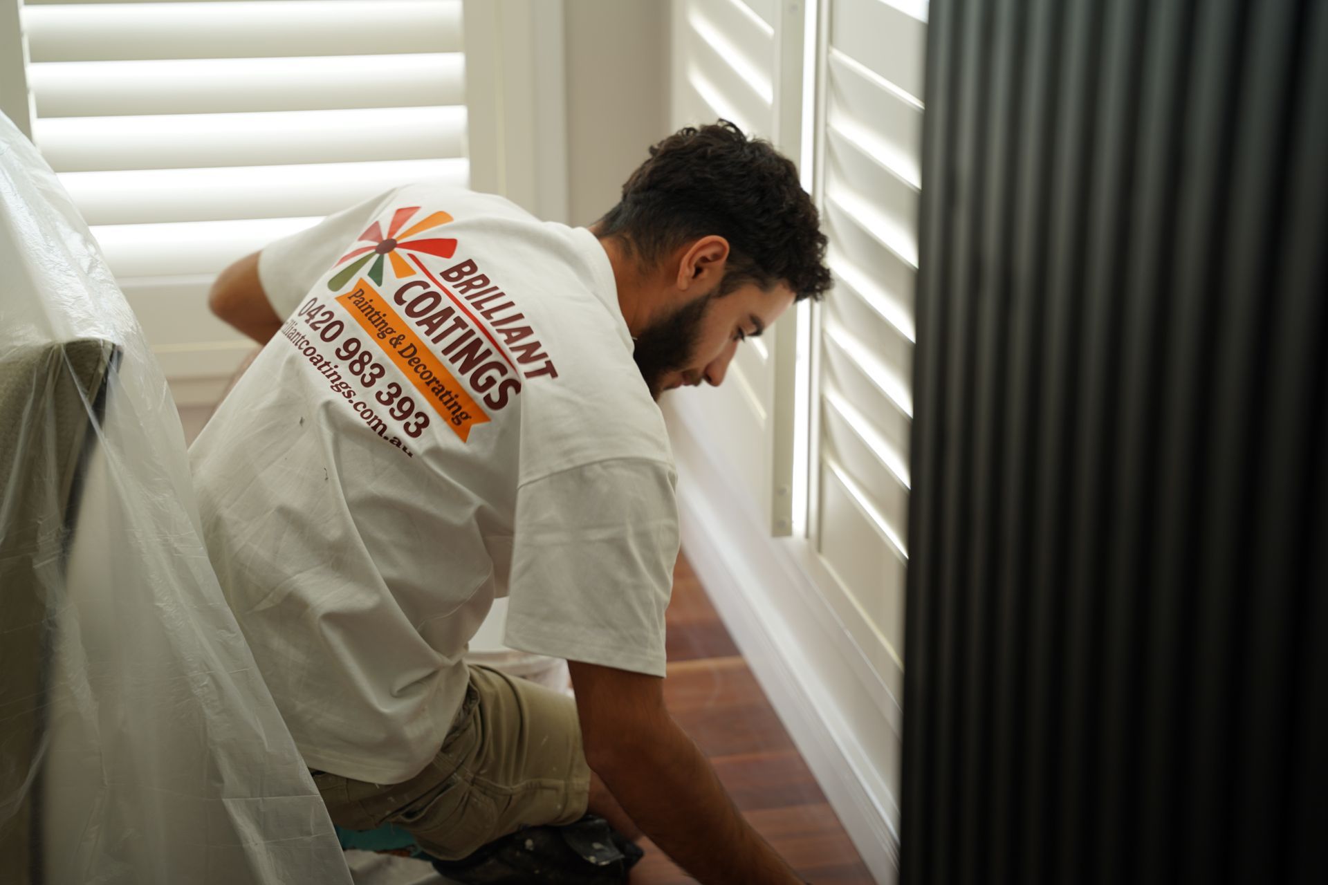 Man painting a white window frame, wearing a white shirt with a Brilliant coatings logo on his shirt.