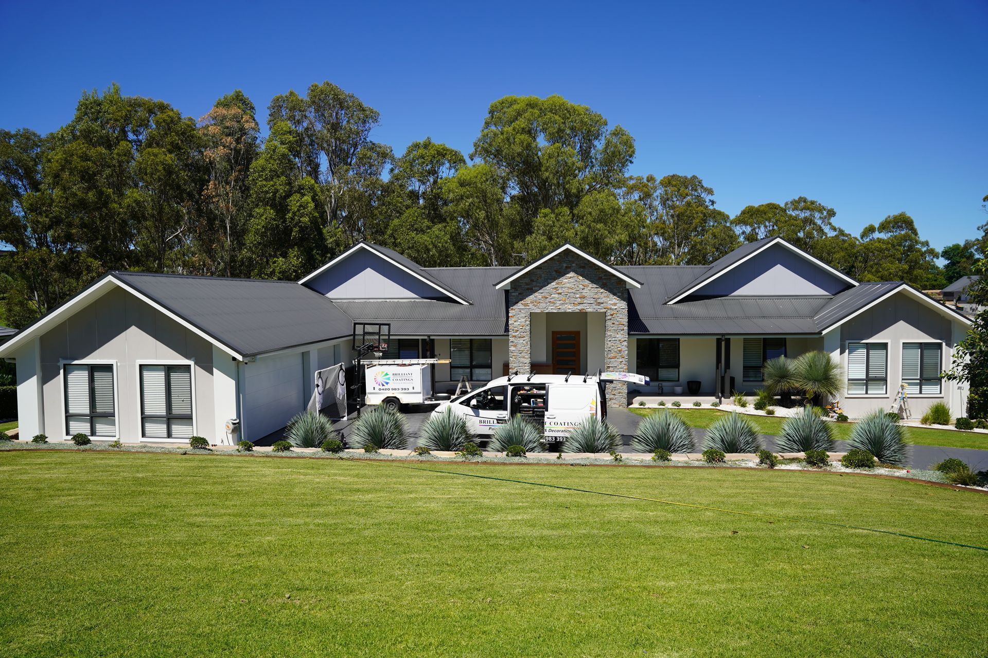Large modern house with gray roof and stone facade; white service van parked in front.