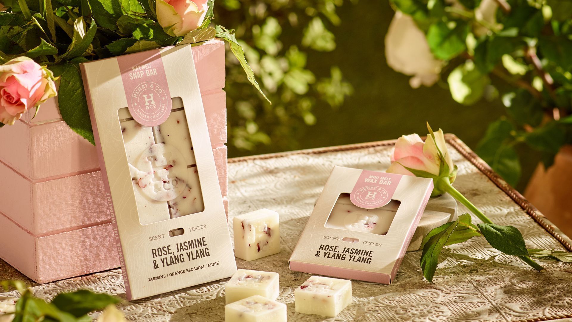 Lit candle, flowers, and soap on a rustic table in a garden setting.