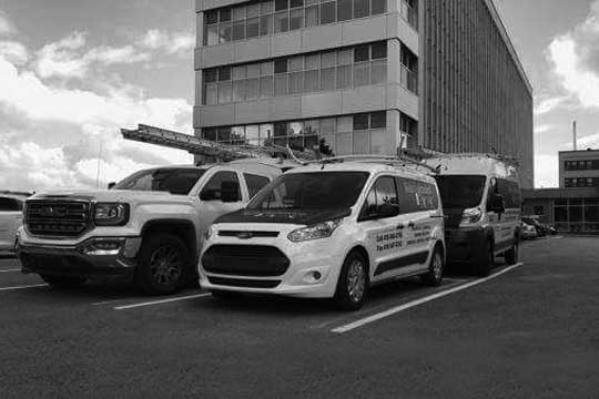 Trois camions et une camionnette sont garés sur un parking devant un immeuble.