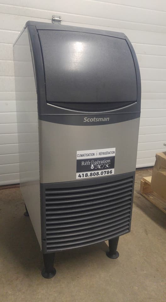 Une grande machine à glaçons est posée sur le sol devant une porte de garage.