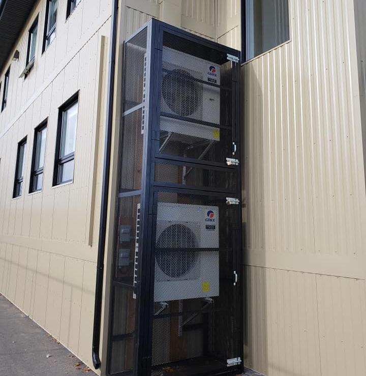 Unités de climatisation encastrées dans une cage métallique noire à l'extérieur d'un bâtiment.