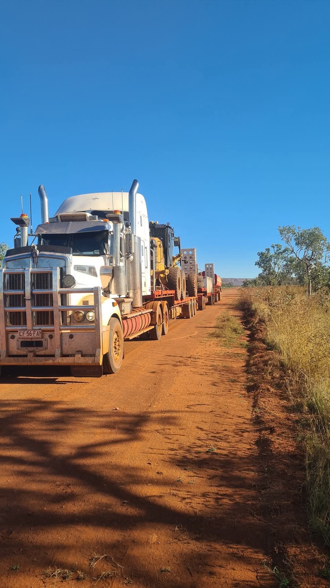 White semi-trucks with trailers parked on a dirt road under a clear blue sky.