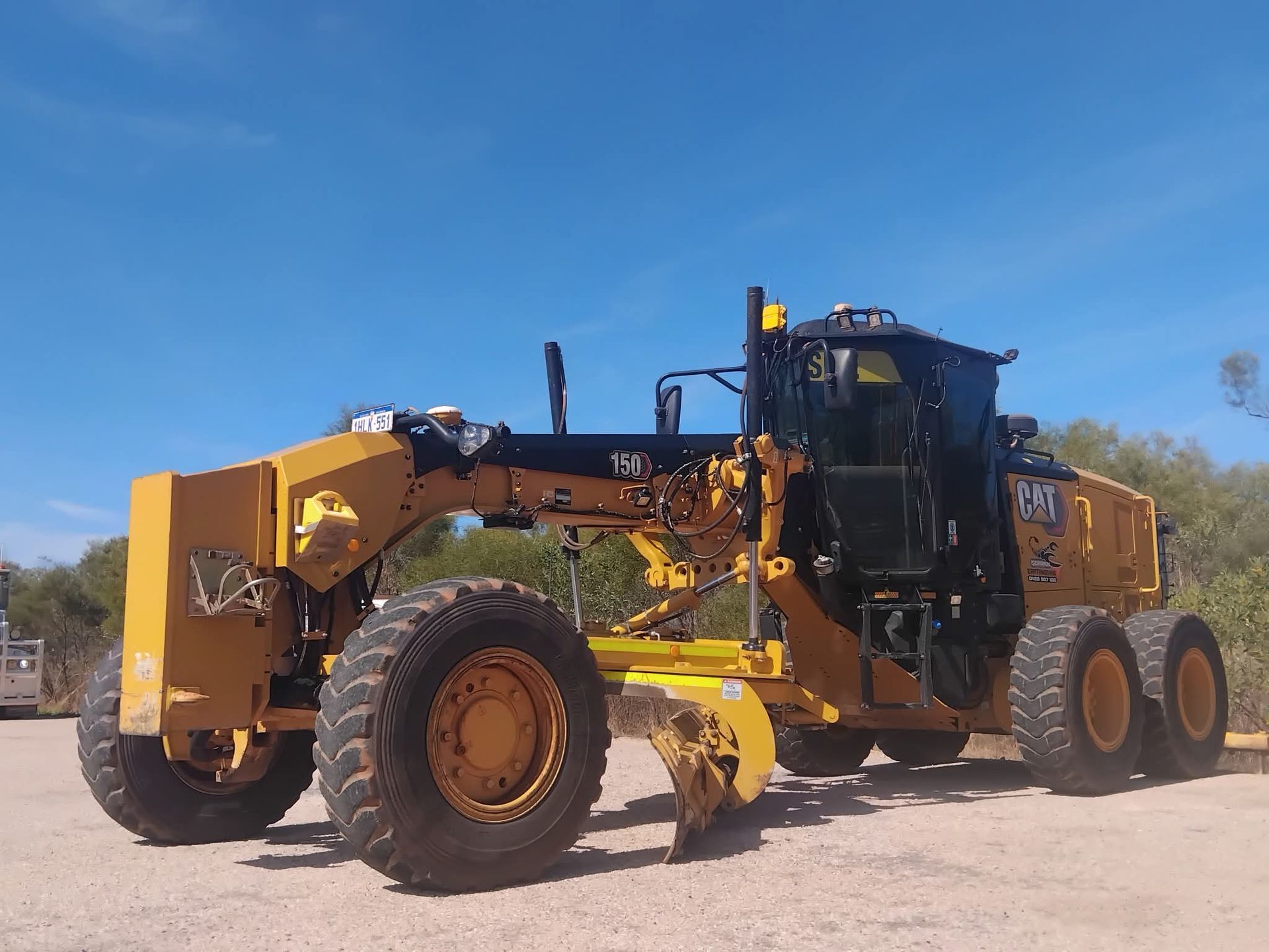 Yellow Caterpillar motor grader on a paved surface, blue sky background.