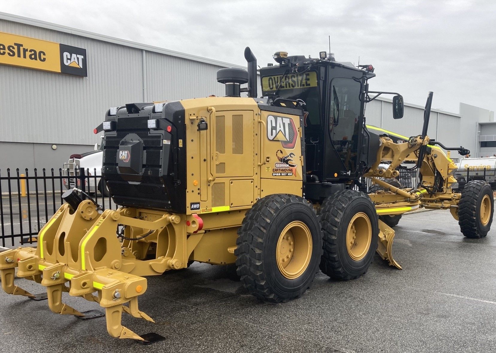 Yellow Caterpillar grader parked outside a building.