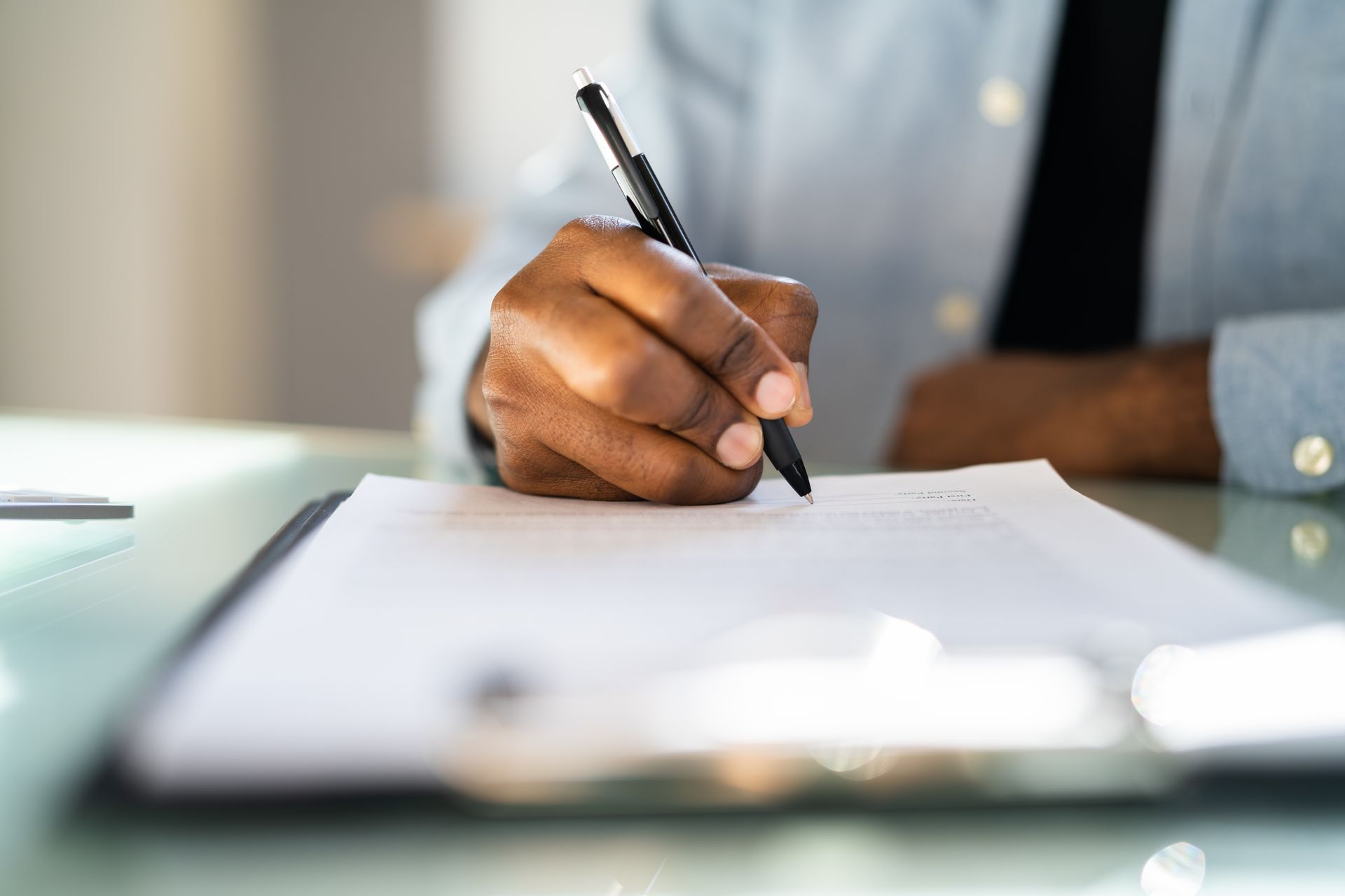 Person's hand writing with a pen on paper attached to a clipboard, close-up shot.