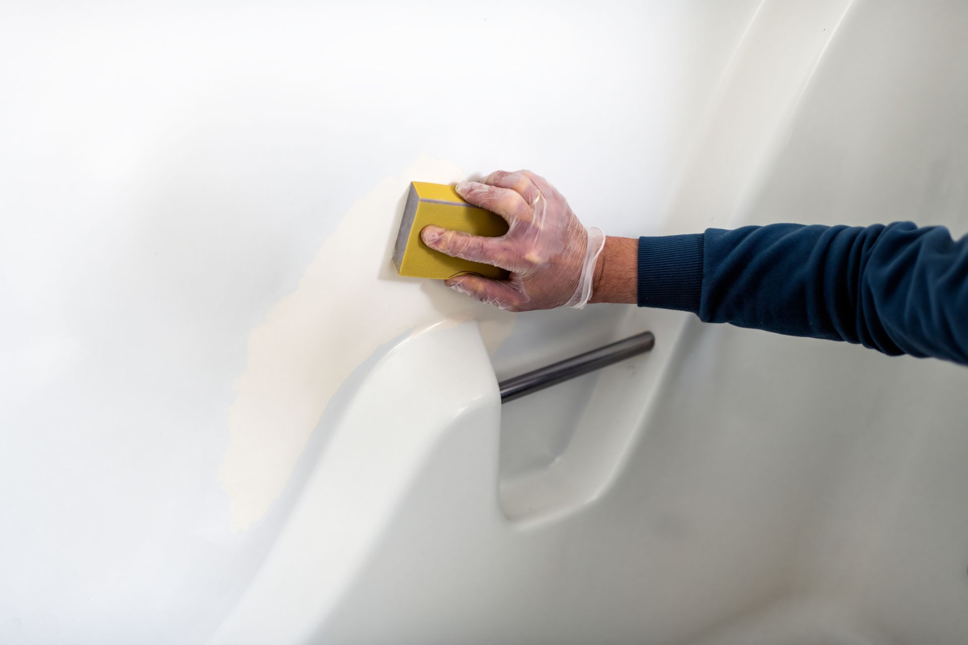A person is cleaning a bathtub with a yellow sponge.