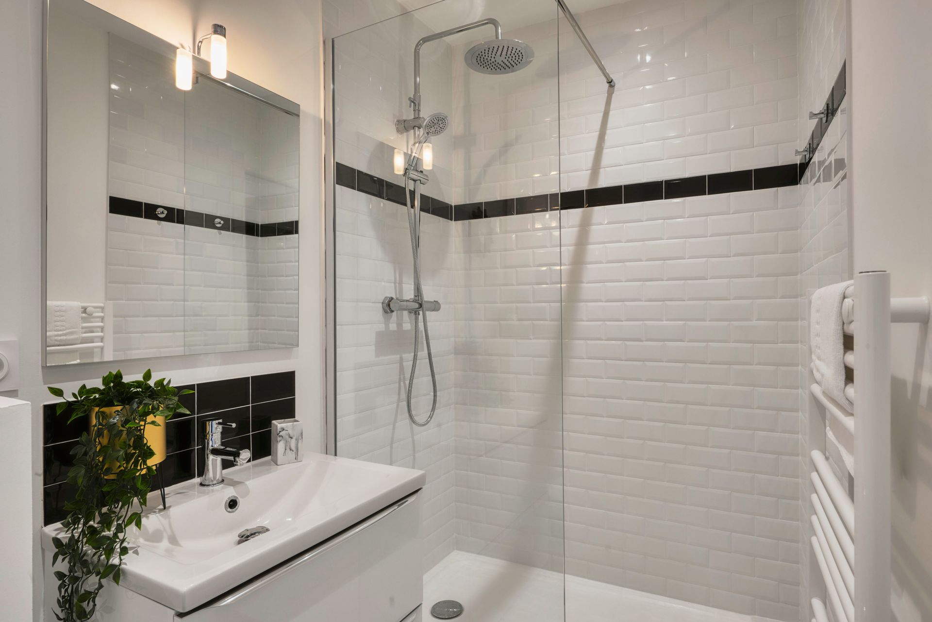 A bathroom with a walk in shower , sink , mirror and towel rack.
