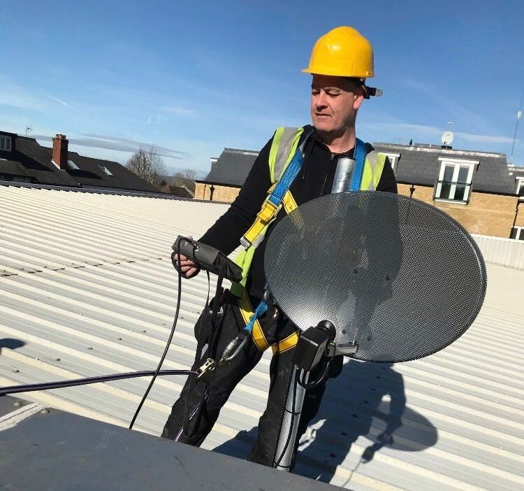 Adult male installer attaches a satellite dish to a roof.