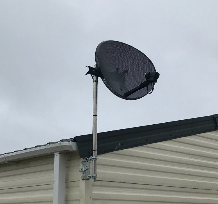 Satellite dish fixed to a pole at the base of a house roof.