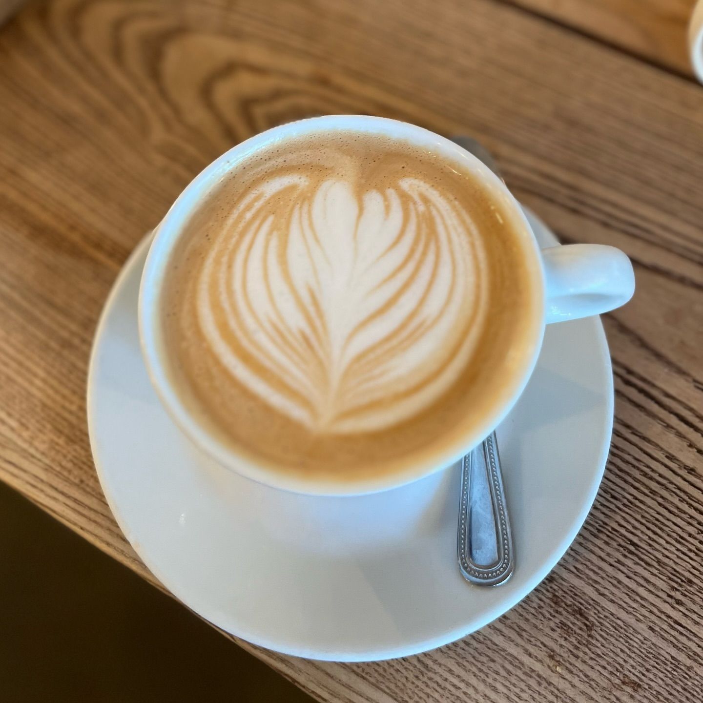 Two lattes on saucers with heart-shaped foam art; spoons rest nearby, set on a wooden table.