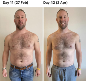 A man without a shirt is standing in front of a white wall.