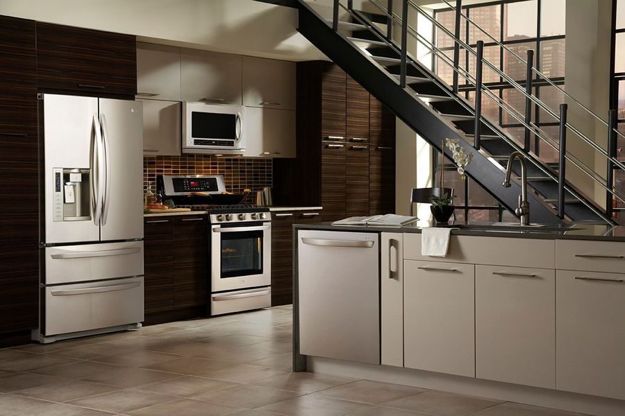 Modern stainless steel appliances in a kitchen with dark wood cabinets, light-colored countertops, and an open staircase.