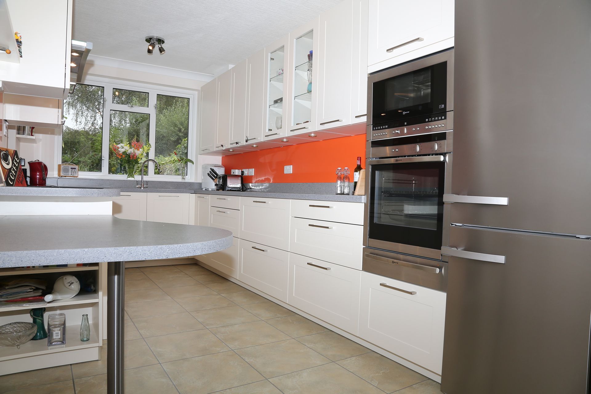 A kitchen with white cabinets, a bright orange backsplash, grey countertops, stainless steel appliances, and tiled floors.