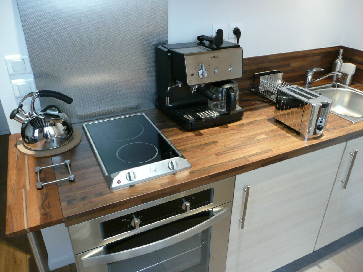 Kitchen counter with a metal kettle, stovetop, coffee machine, toaster, and sink on a wooden surface with white cabinets.