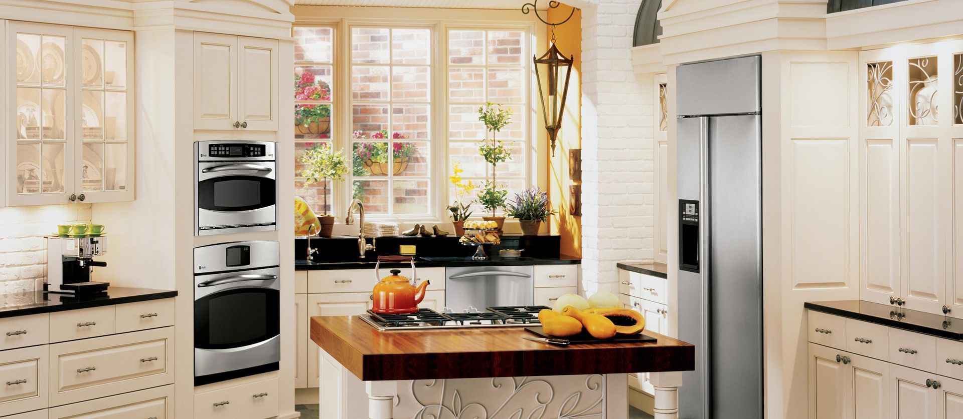 A cream-colored, traditional-style kitchen with stainless steel appliances, a center island, and large windows.