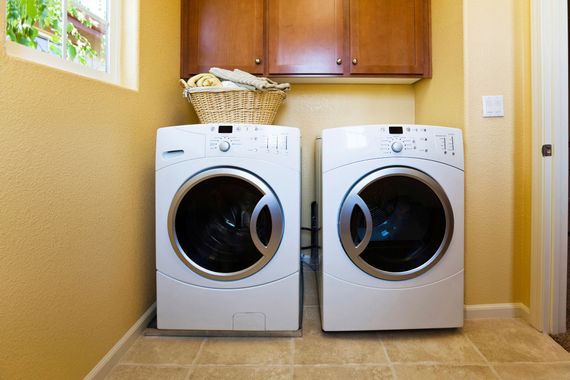 A white washer and dryer sitting side-by-side in a laundry room with tan walls and wooden cabinets above.