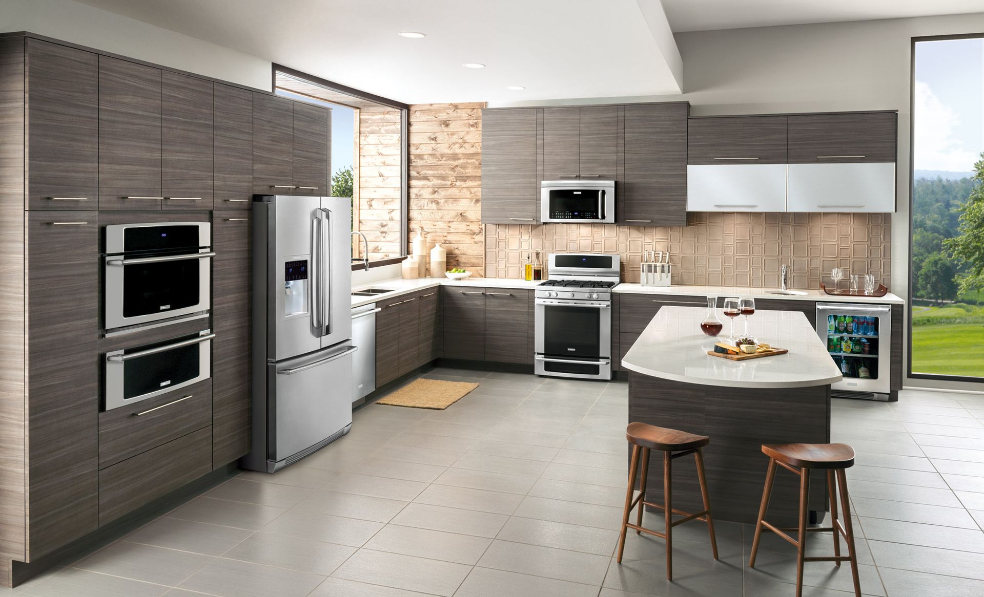 Modern kitchen with dark wood cabinets, stainless steel appliances, a white island with two stools, and large windows.