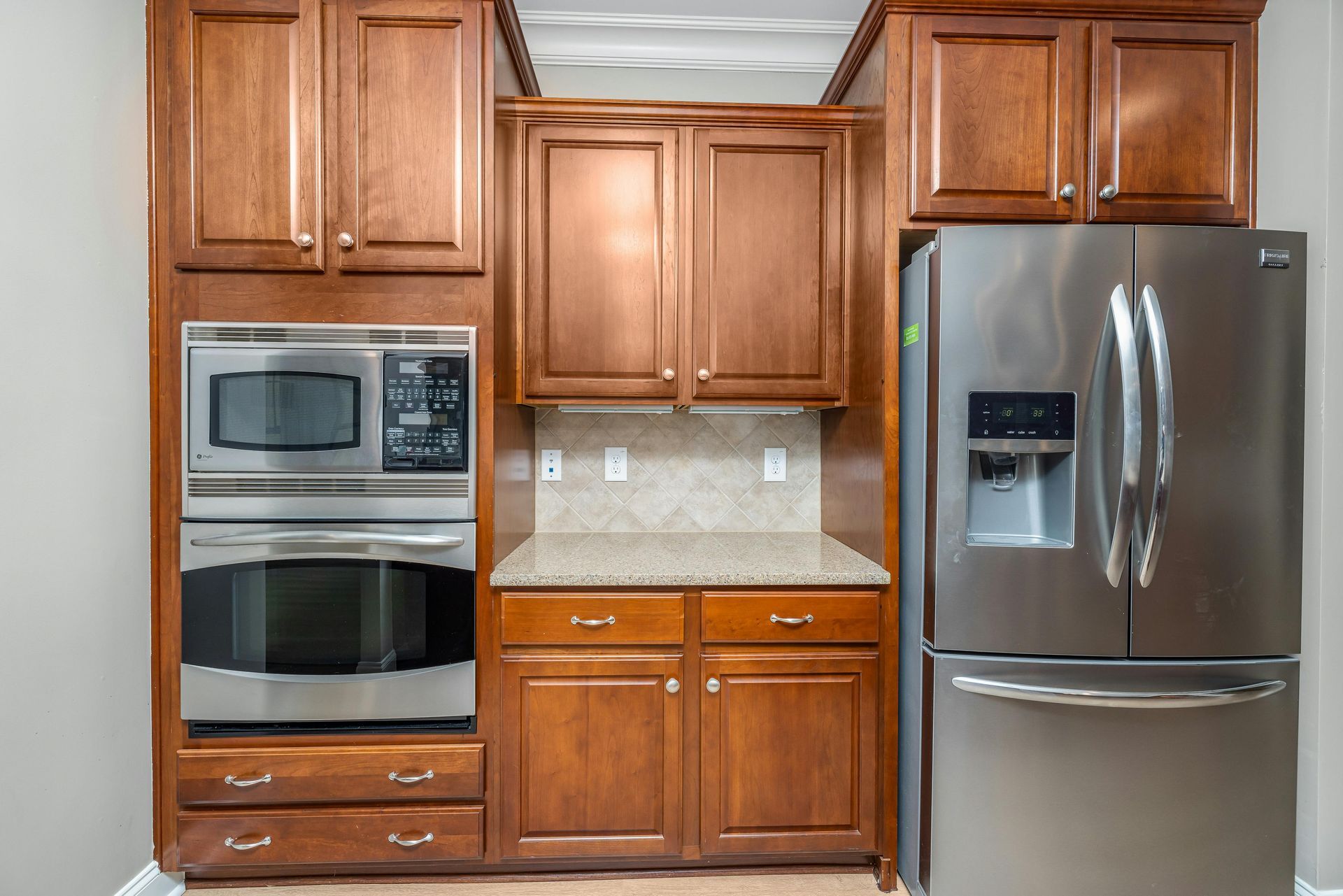 A kitchen wall featuring wood cabinets, a built-in microwave and oven, a countertop area, and a stainless steel refrigerator.