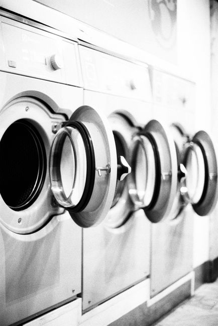 A row of industrial clothes dryers with their round doors open, captured in a black-and-white, slightly blurred style.