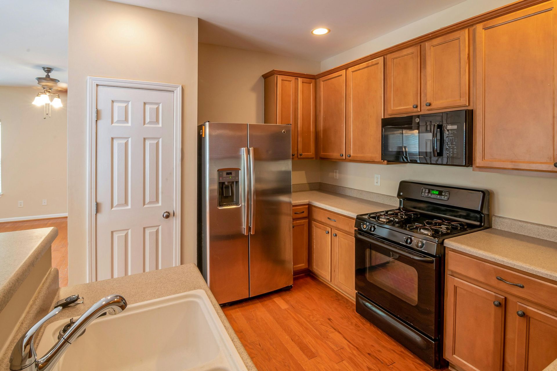 A kitchen with light wood cabinets, stainless steel appliances, a black gas stove, and a white sink on a countertop.