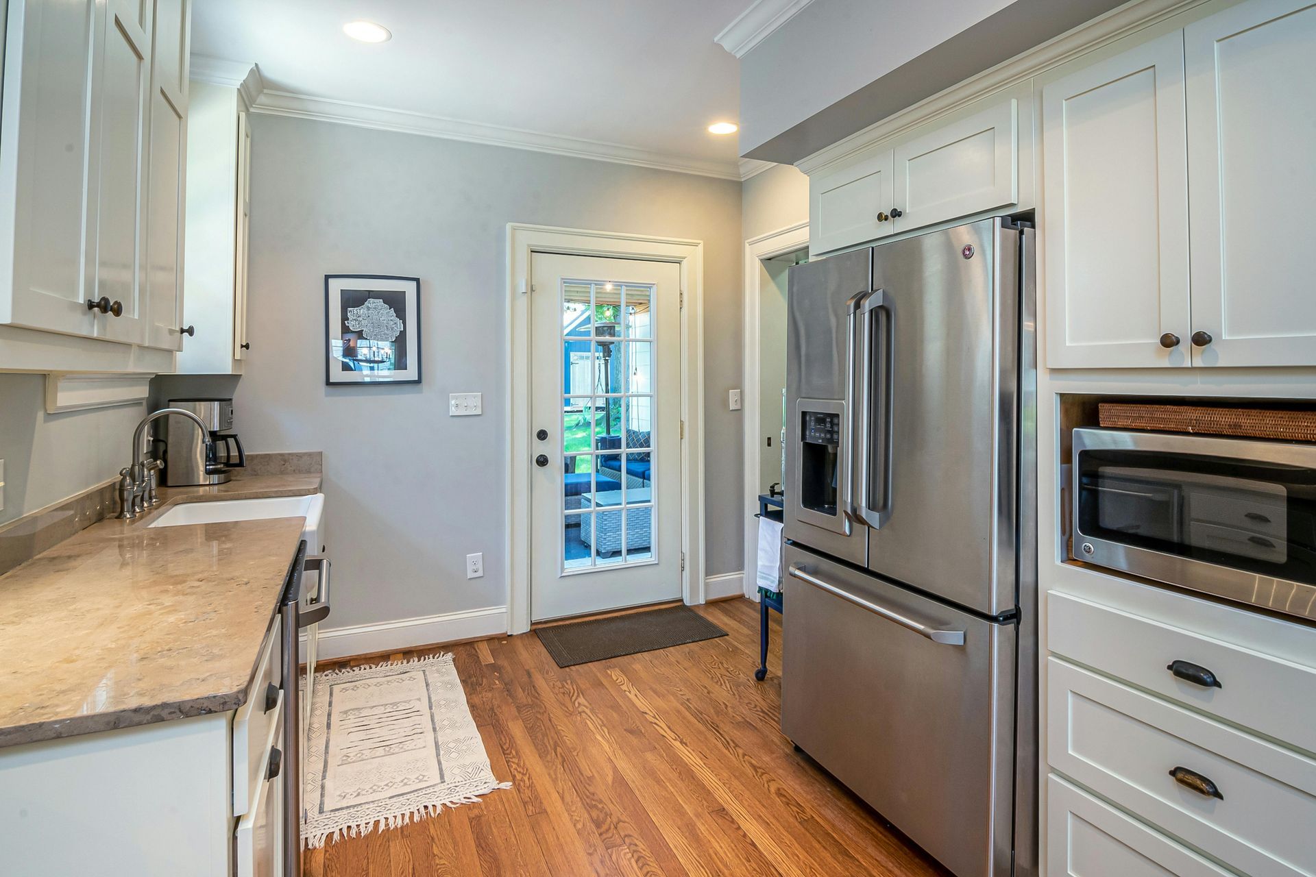 A bright kitchen features white cabinets, granite countertops, stainless steel appliances, and wood flooring.