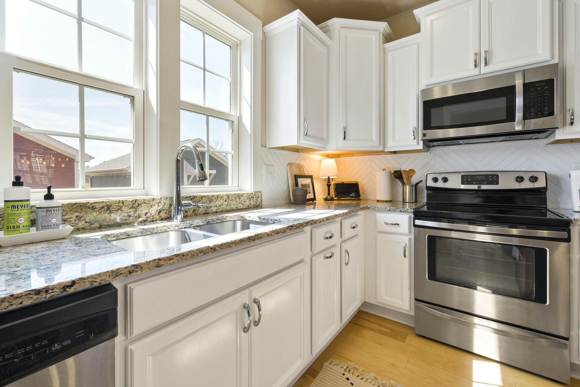 A bright kitchen with white cabinets, speckled granite countertops, stainless steel appliances, and a double window.