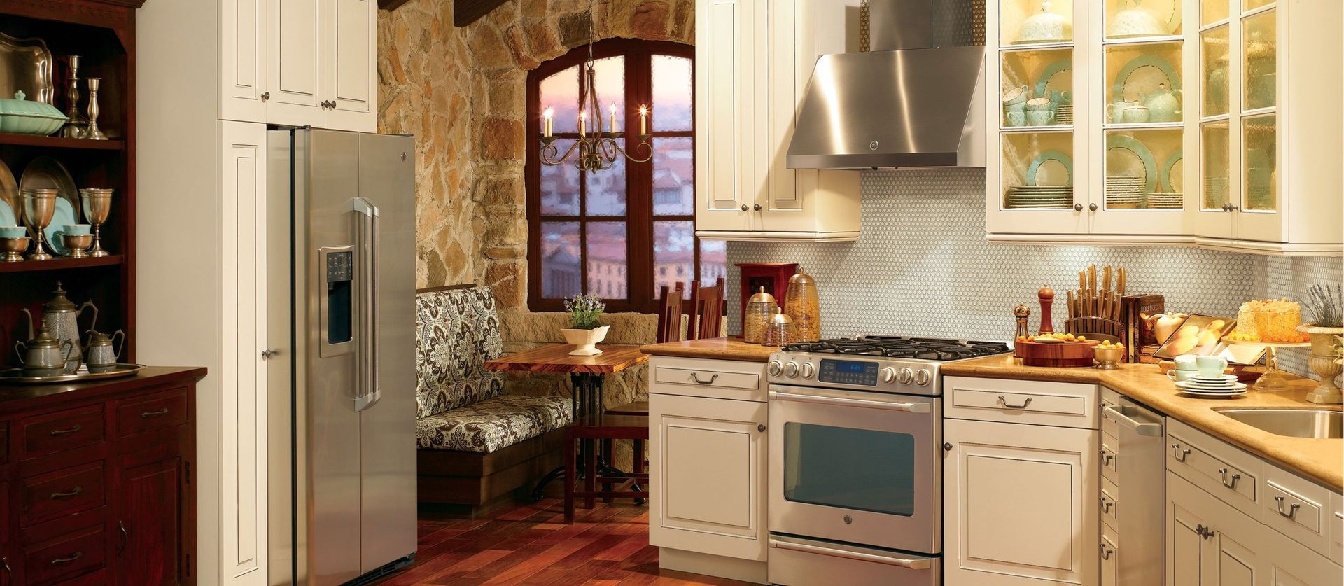 A bright kitchen with white cabinets, stainless appliances, stone walls, a small breakfast nook, and wooden floors.
