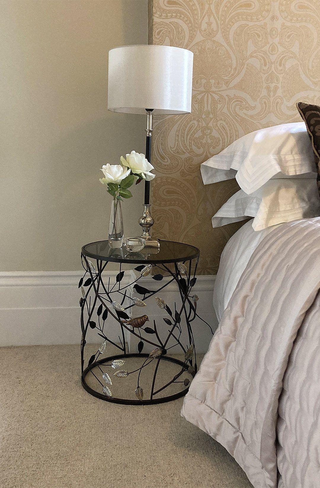 Small round metallic table with leafs and birds decoration with lamp on top closeup interior design