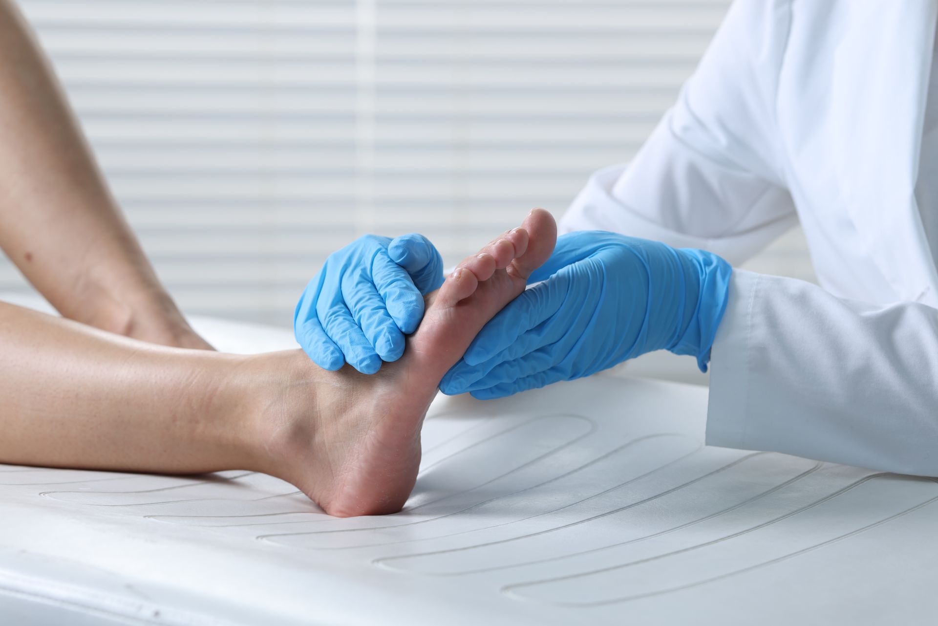 A healthcare provider in blue gloves examines a patient's foot on a white examination table.
