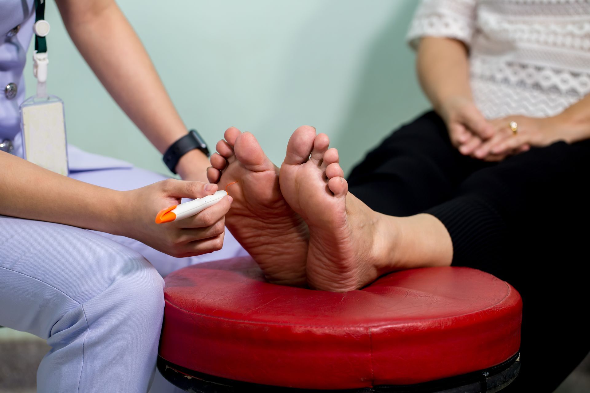 Nurse examining a patient's feet with a pen while seated on a red stool.