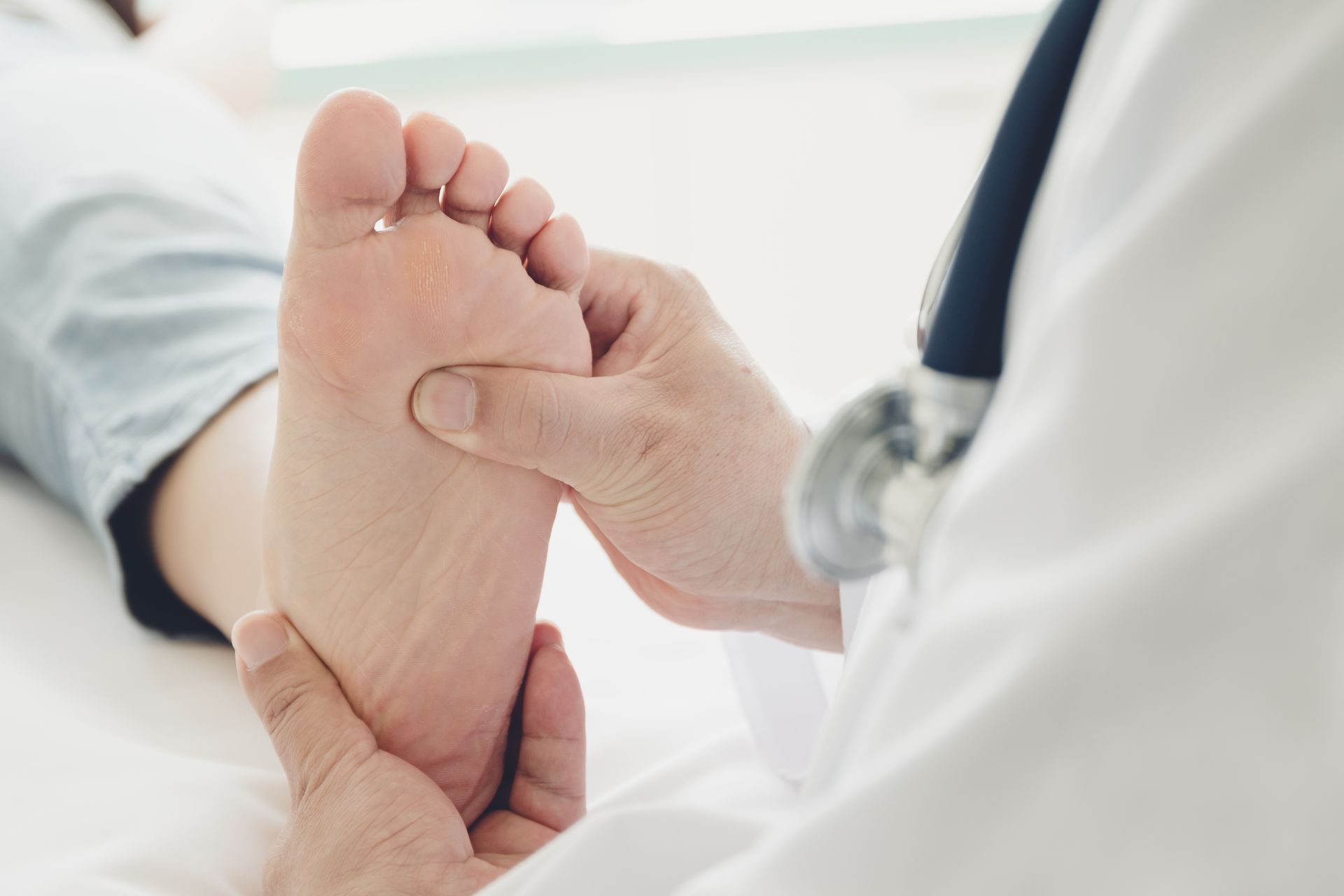 Doctor examining a patient's foot on a medical exam table with a stethoscope visible.