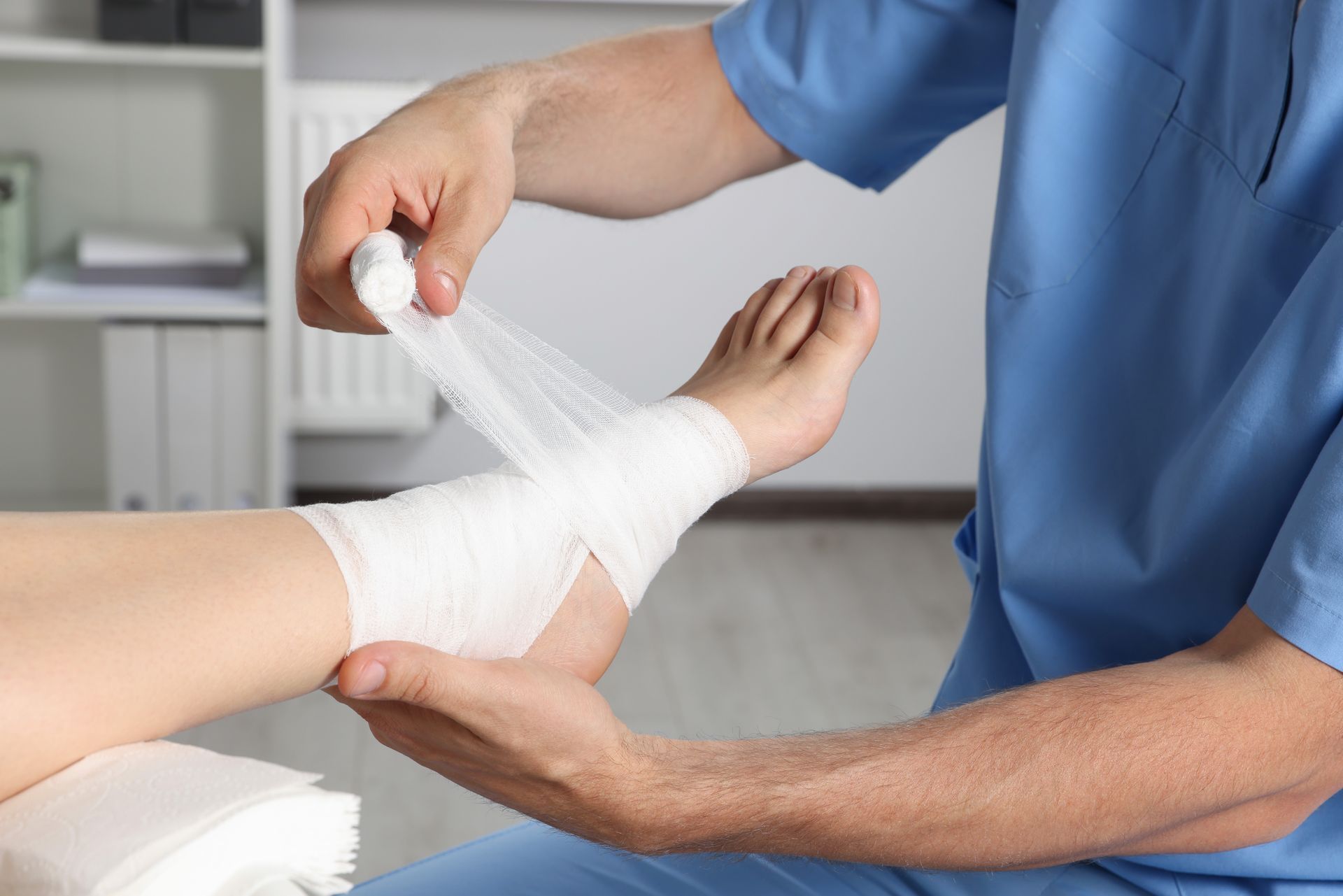 A healthcare worker wraps a bandage around a patient's injured ankle indoors.