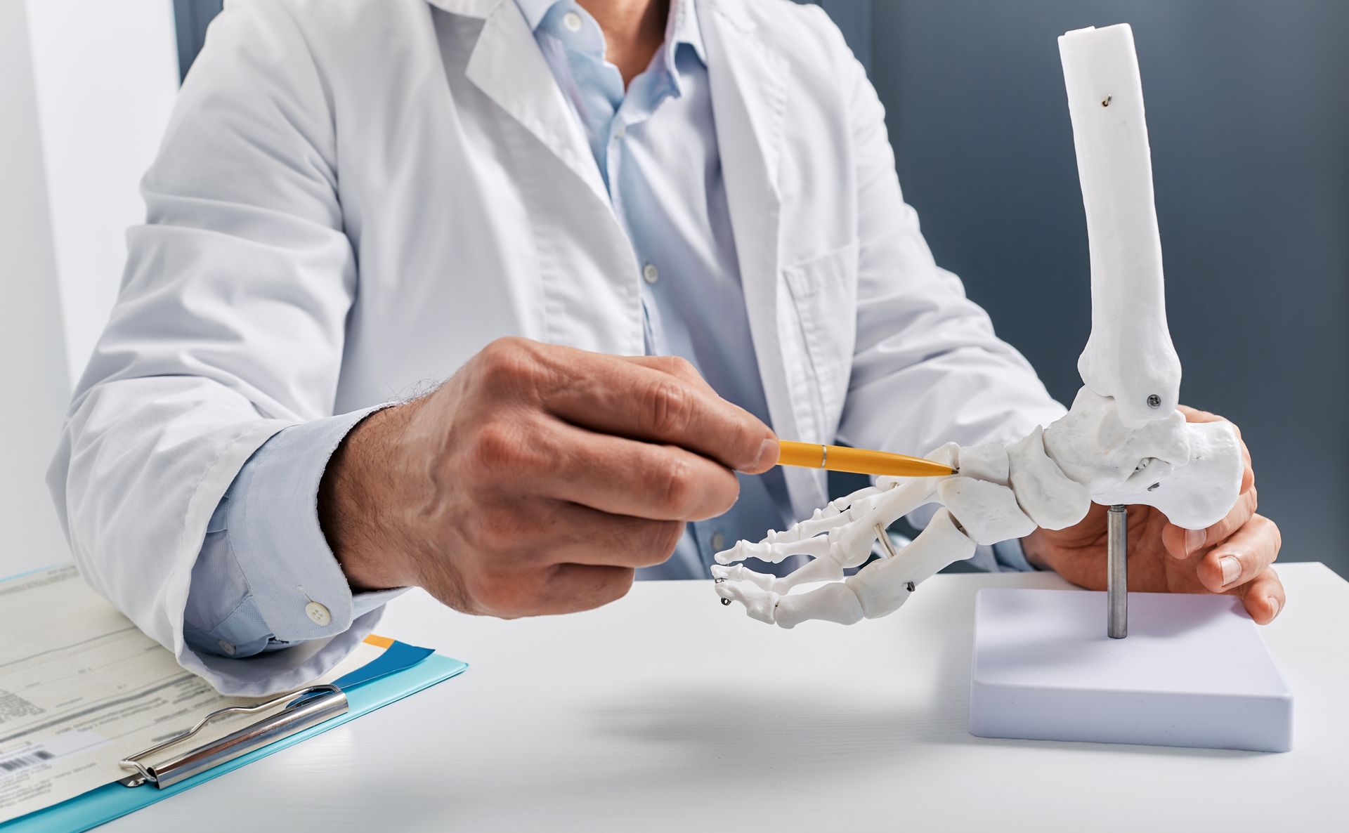 Doctor pointing a pencil at a foot bone model on a table.